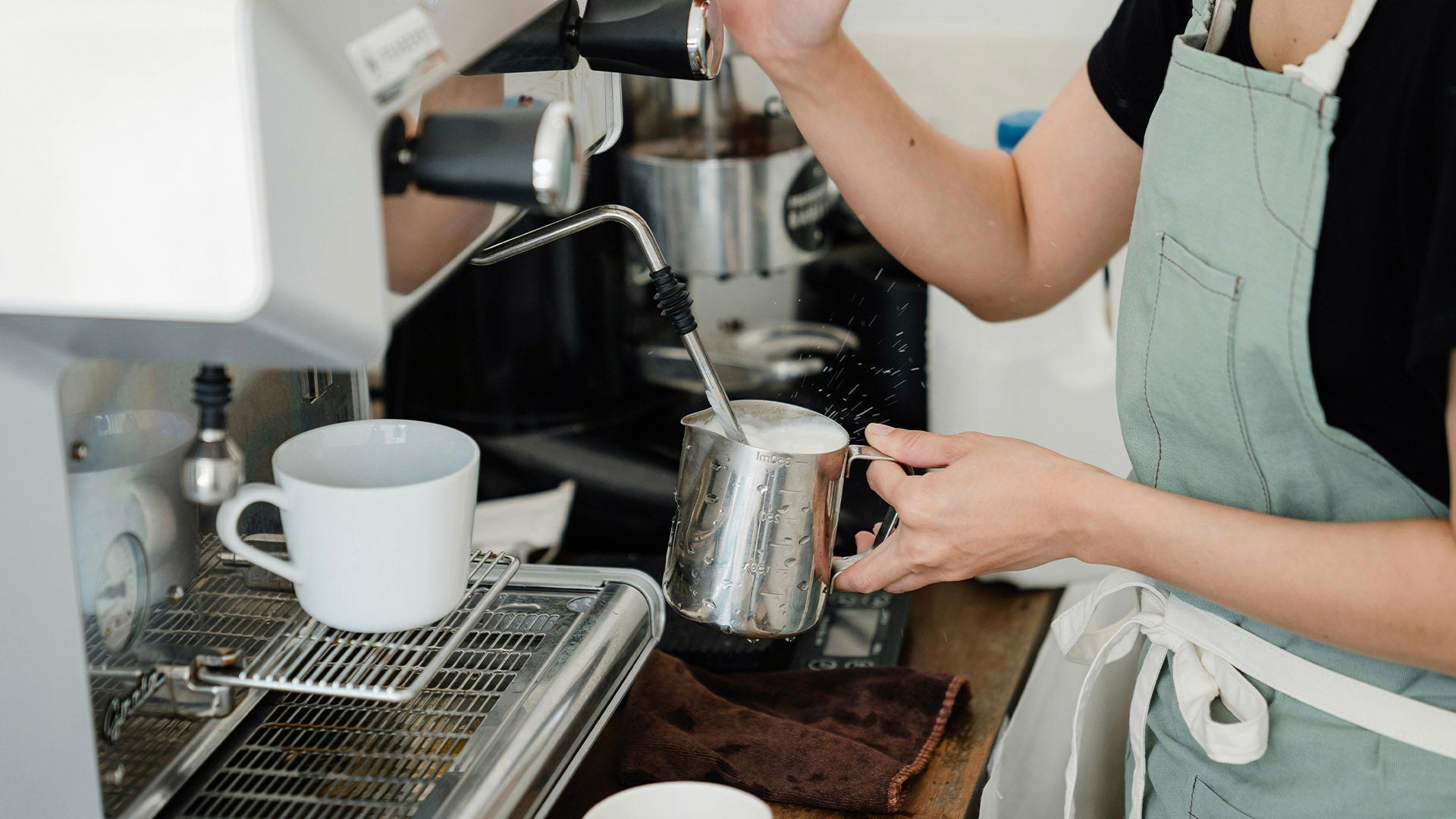 Barista steaming milk in a stainless pitcher using a professional espresso machine