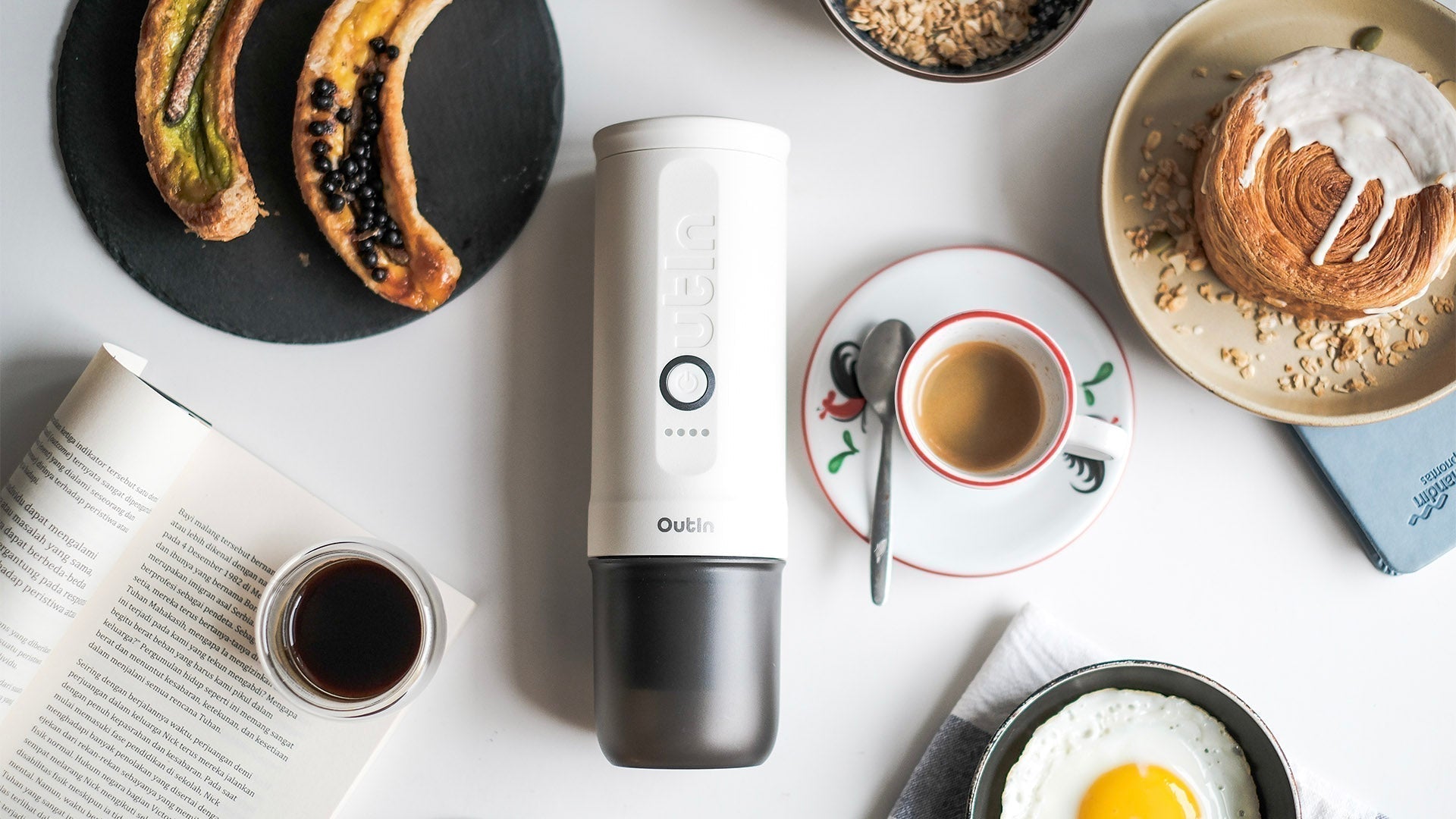 Outin portable espresso maker with healthy breakfast spread and coffee on white marble countertop