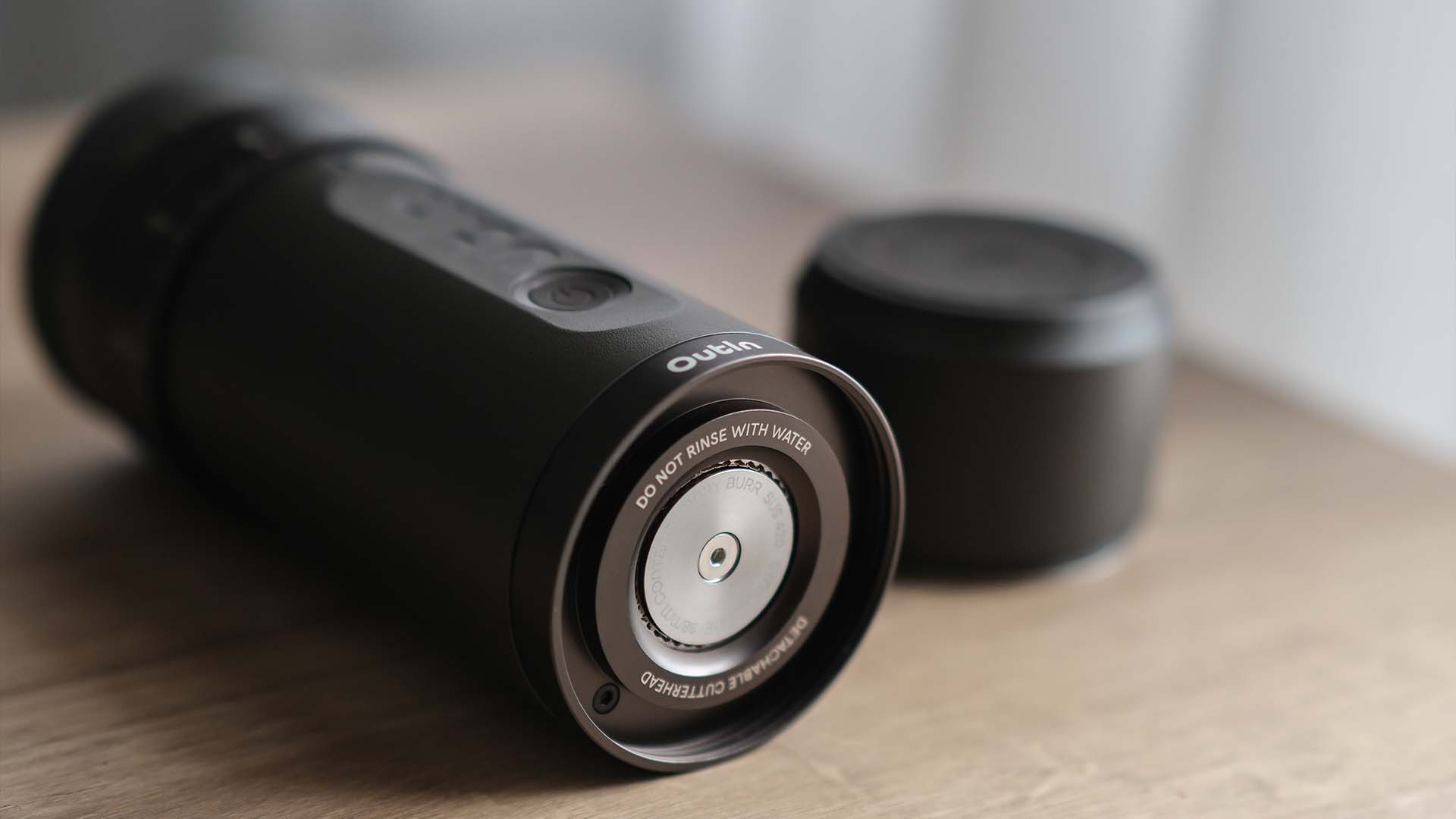 Close-up of a portable electric coffee grinder lying on a wooden table, showing the metal burr and minimalist design