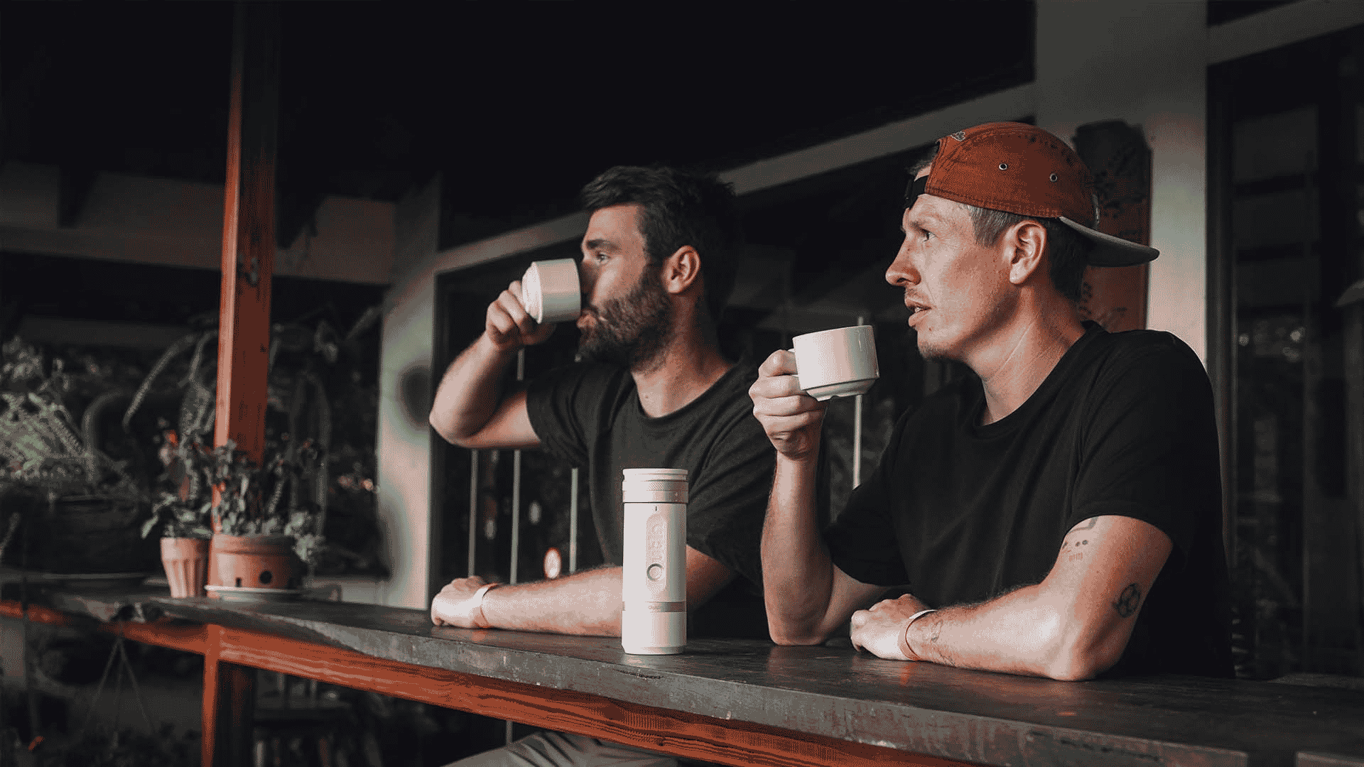 Two people drinking coffee with a portable espresso machine on the table during an afternoon break