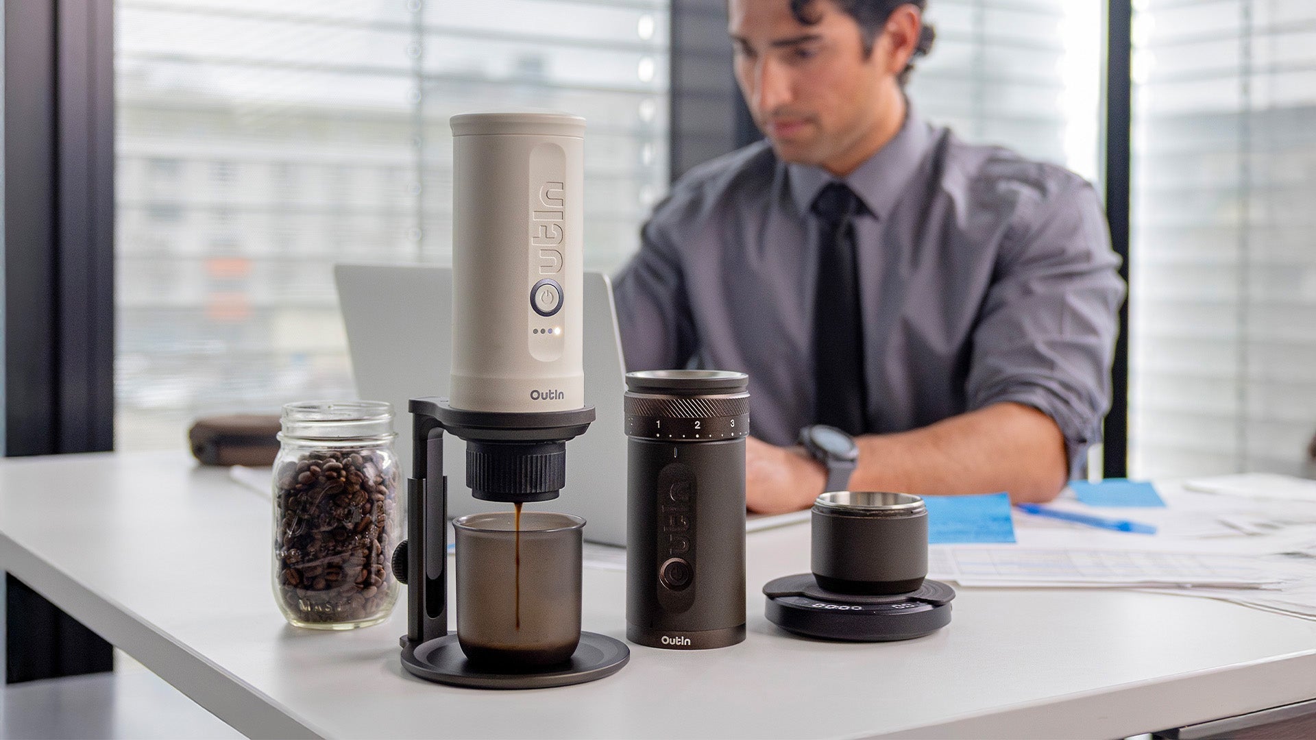 The Outin Portable Espresso Machine and accessories on an office desk, illustrating premium, on-the-go coffee for the busy professional