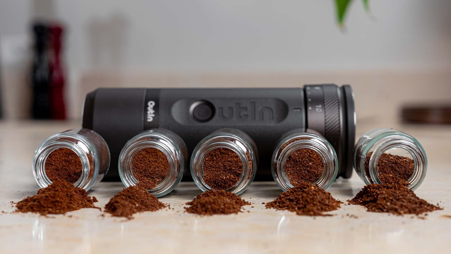 Portable espresso maker with six small jars showing different espresso grounds piles on a kitchen counter.