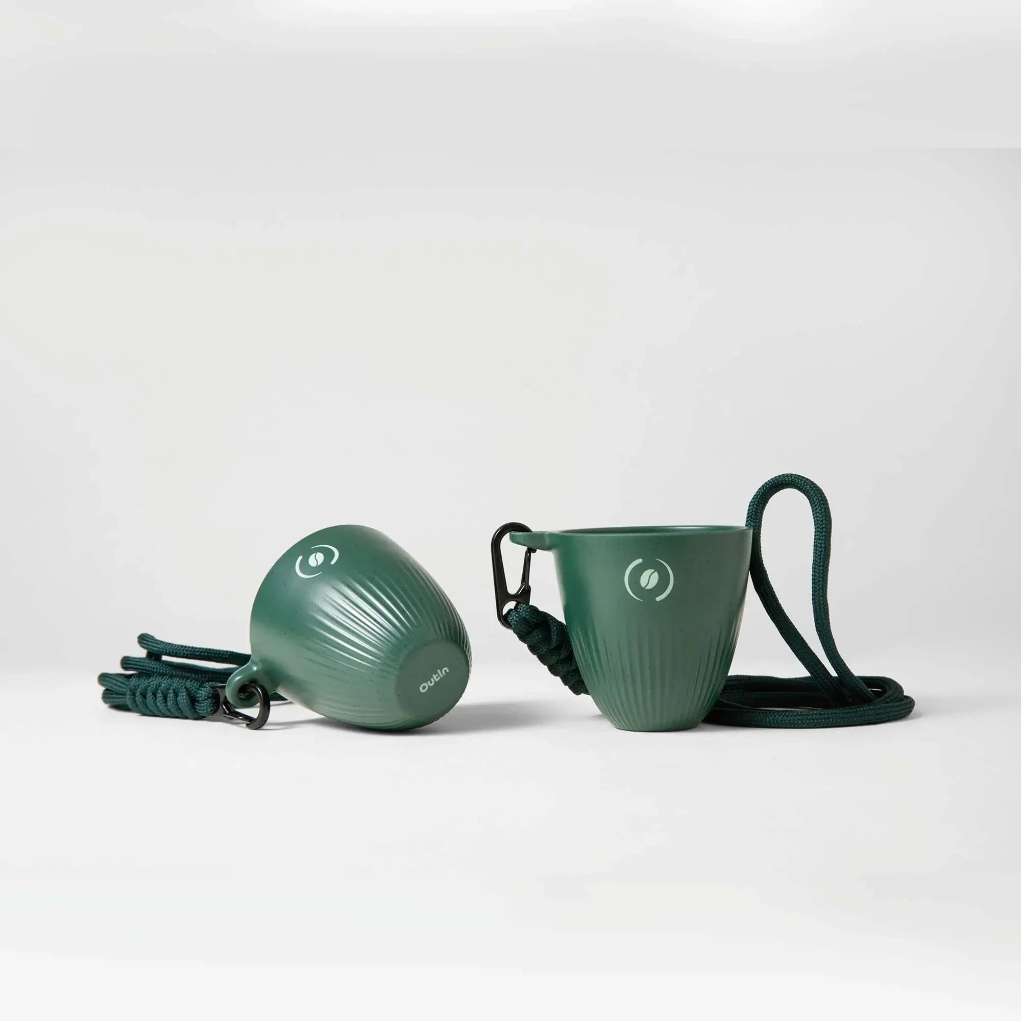 Two dark green OutIn Rebrew ribbed espresso cups with coffee bean logo and lanyard, showcasing design and portability.