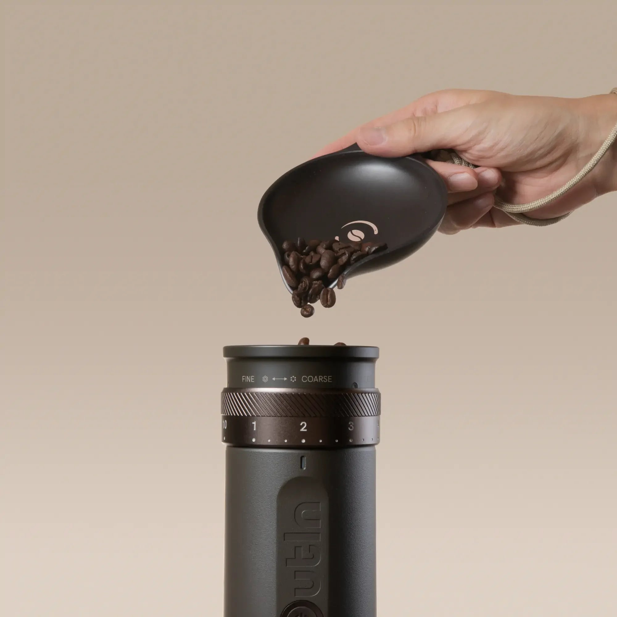 OutIn Rebrew Bean Tray pouring coffee beans into a coffee grinder, with braided lanyard.