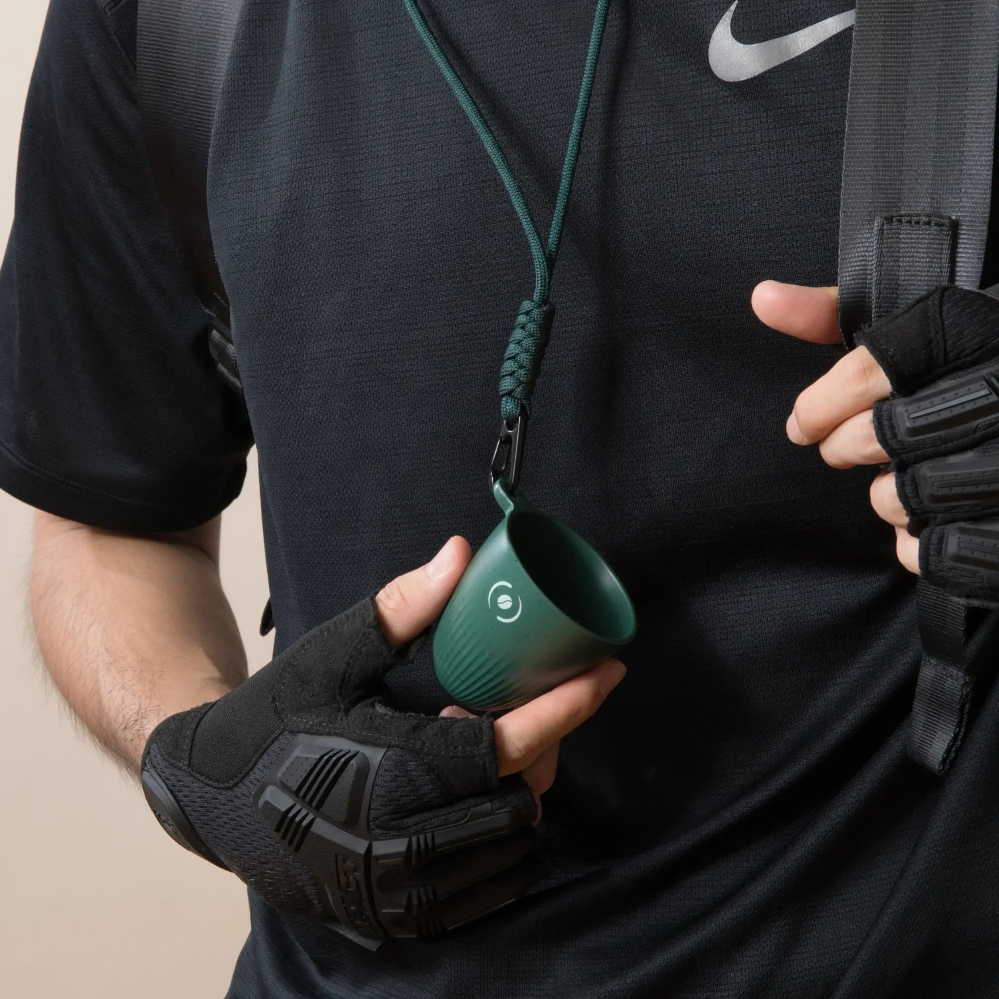 Dark green OutIn Rebrew espresso cup with coffee bean logo, suspended by lanyard for portable, on-the-go use.