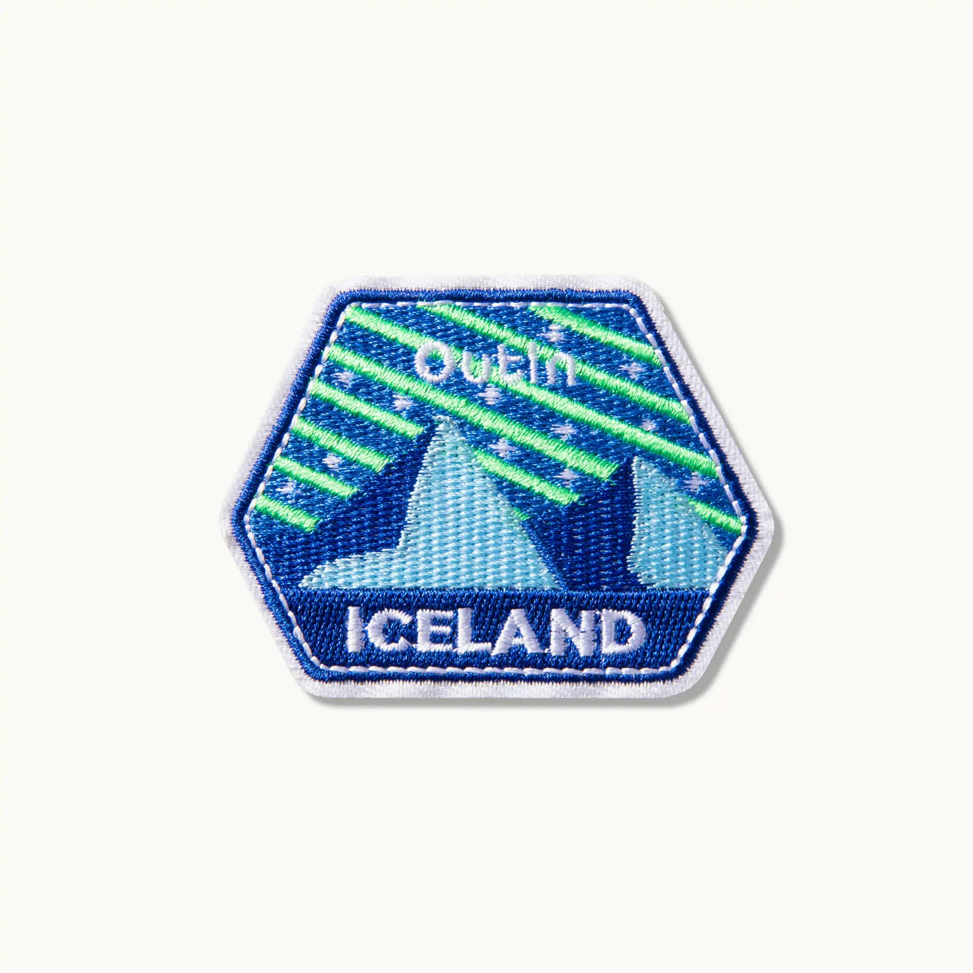 OutIn Iceland hexagonal patch with embroidered aurora borealis over mountains. White 'OutIn' and 'ICELAND' text.