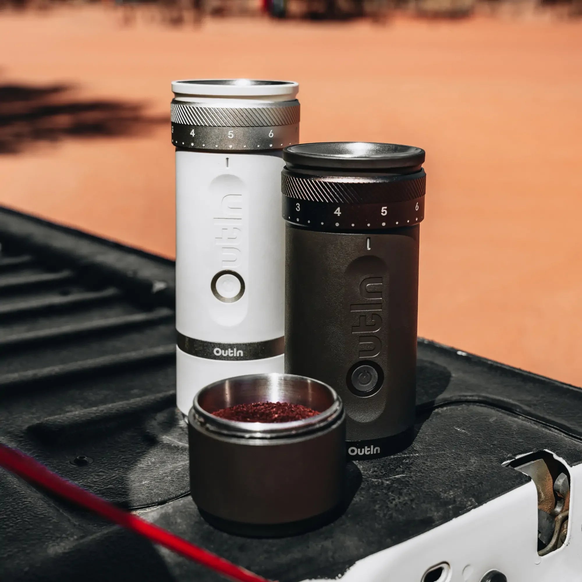 White & dark grey OutIn Fino coffee grinders with grounds, showing colors & portability.