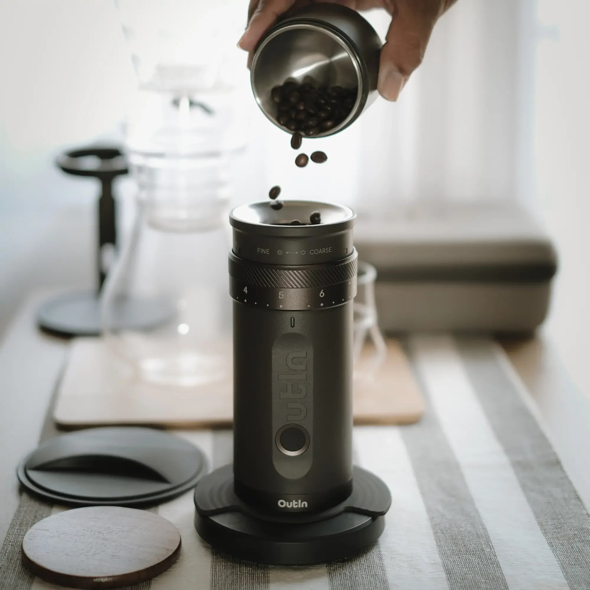Dark grey OutIn Fino portable electric coffee grinder with hand pouring beans, showcasing grind settings and compact design.