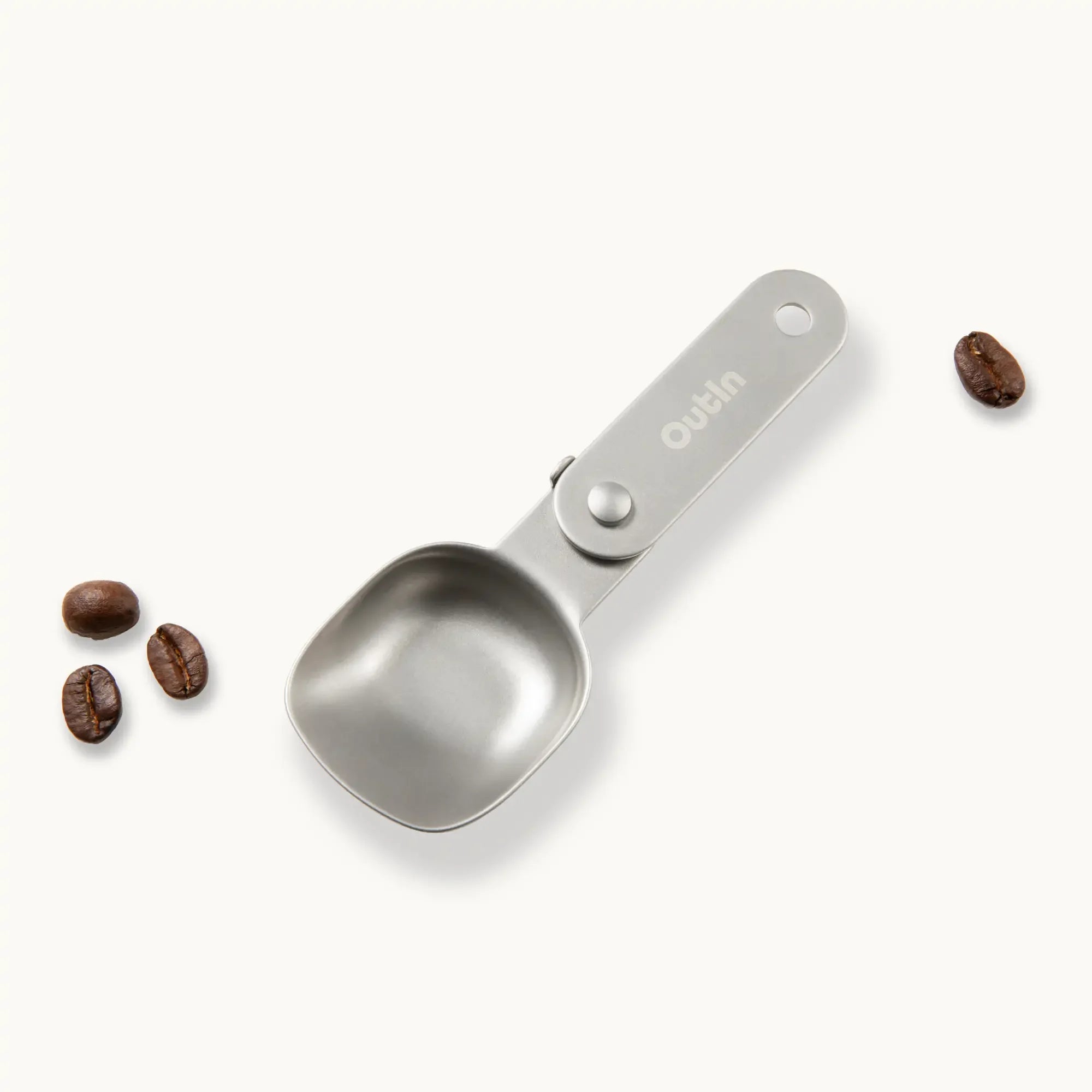 OutIn foldable coffee spoon made of stainless steel with hanging hole and coffee beans.