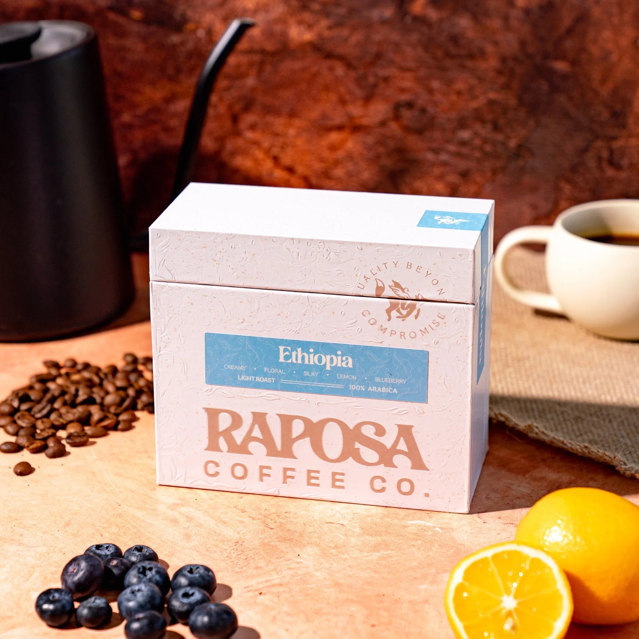 Raposa Coffee Ethiopia Light Roast box with whole beans, blueberries, lemon, and brewing elements.