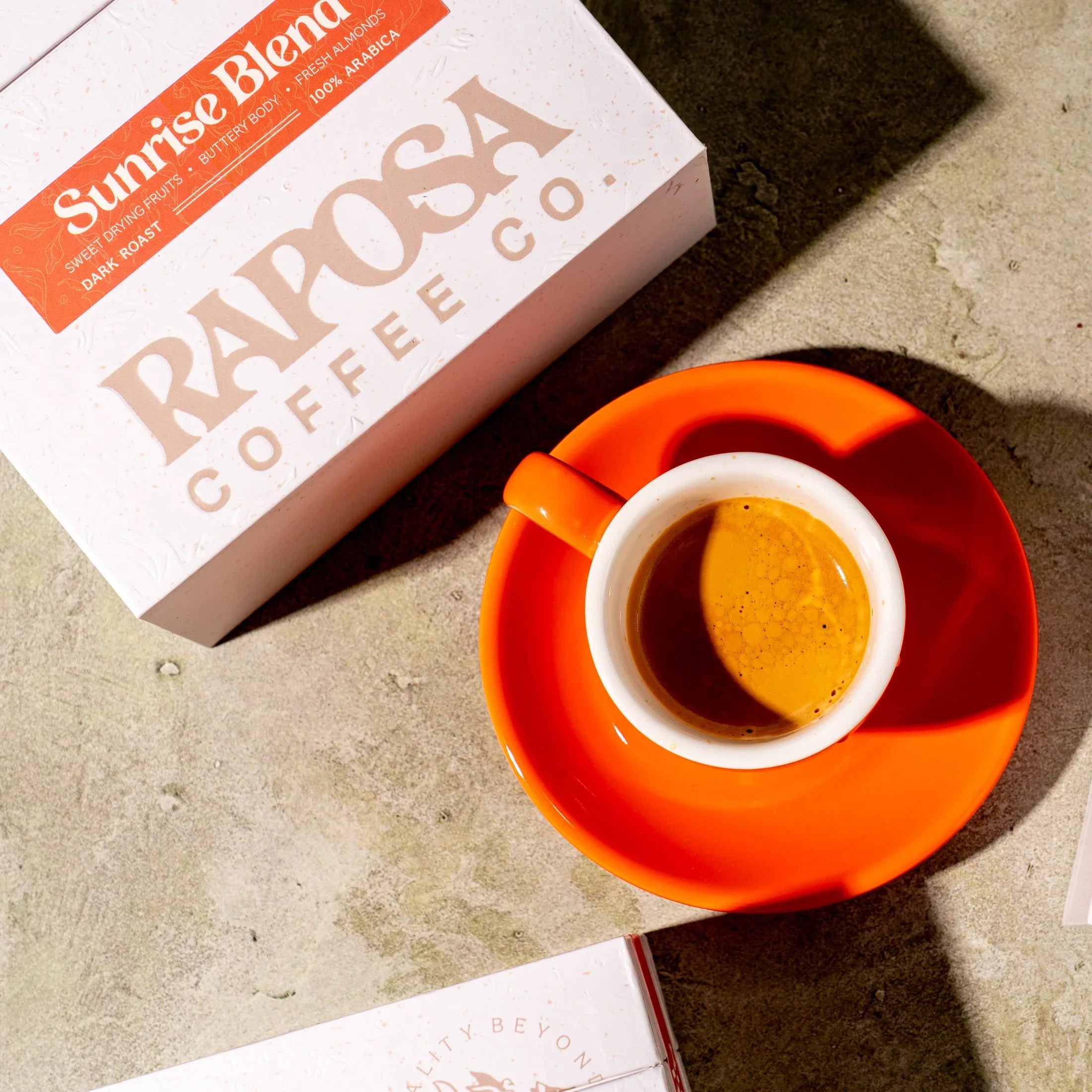 Raposa Coffee Co. Sunrise Blend dark roast whole beans with espresso cup. Notes: sweet drying fruits, buttery body, almonds.