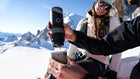 An adventurer brews espresso with an Outin Portable Espresso Machine on a sunny, snowy mountain top