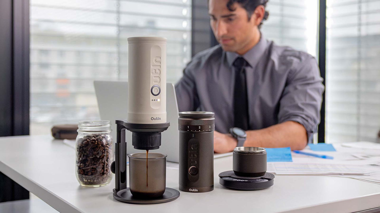 Businessman brewing fresh coffee at office desk with Outin portable espresso machine and grinder, professional workspace coffee setup