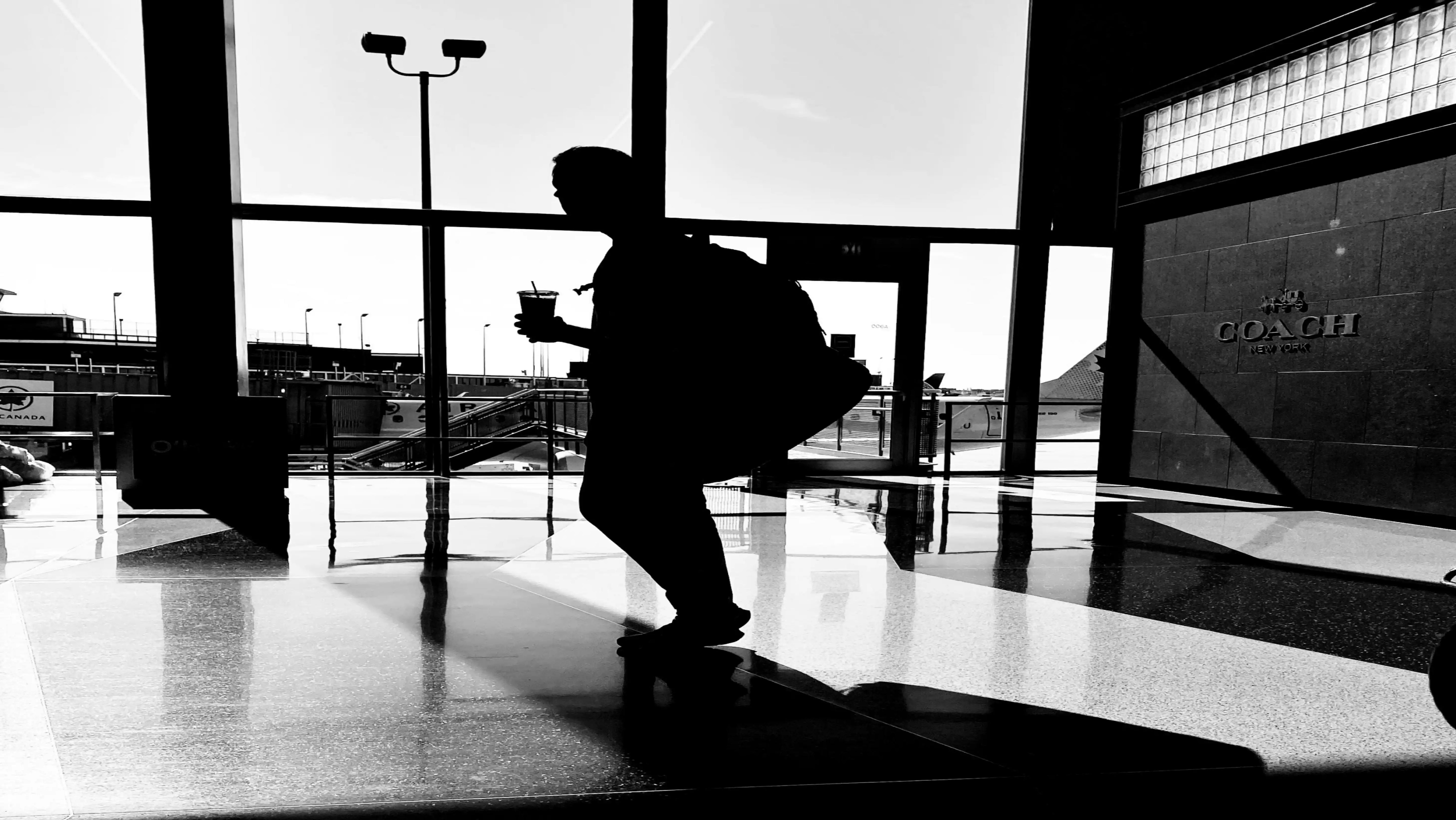 Silhouette of a person walking through an airport with luggage, seen through glass windows.