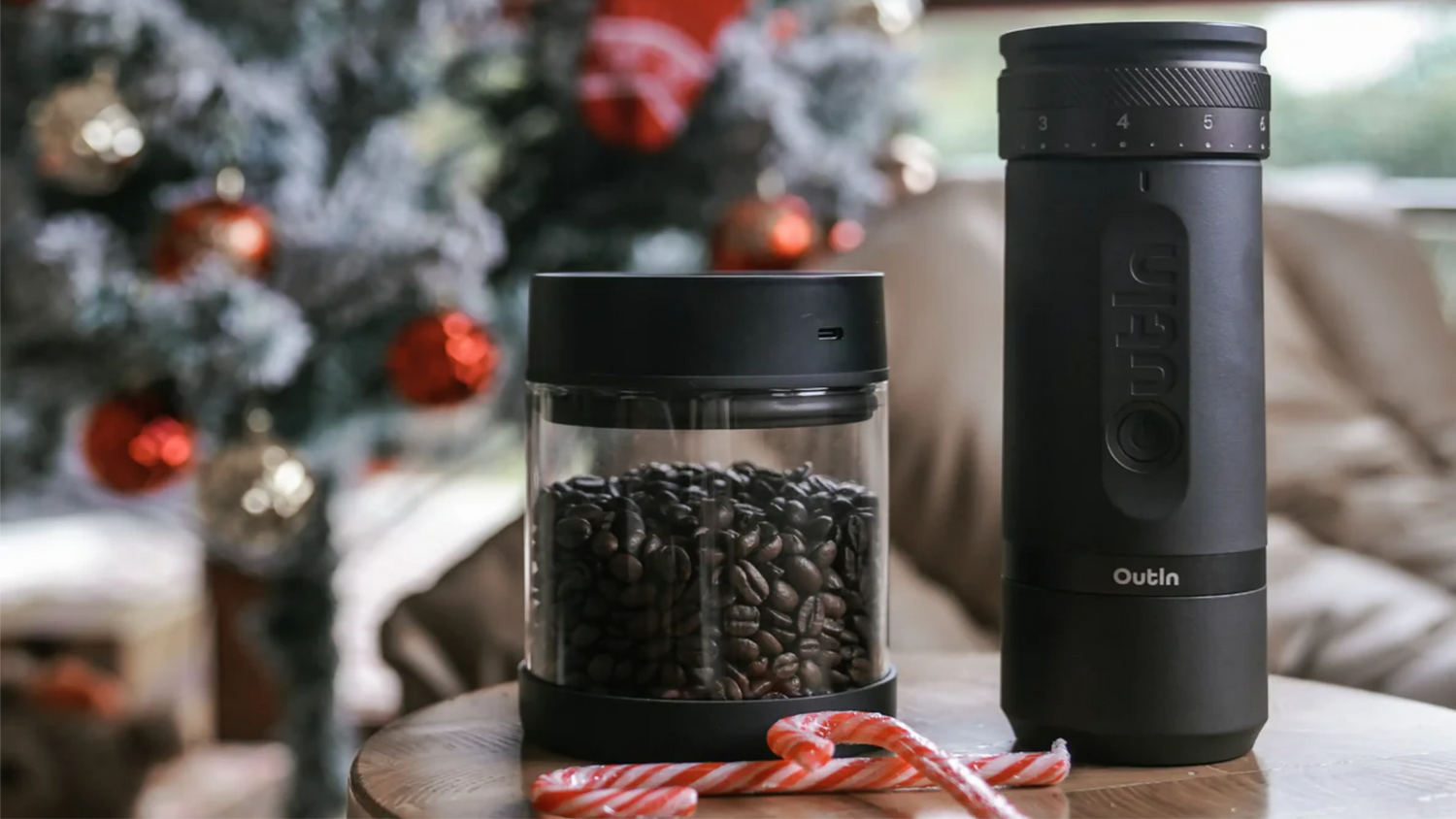 Outin electric coffee grinder and vacuum storage container with fresh coffee beans, displayed against festive Christmas decorations and candy canes