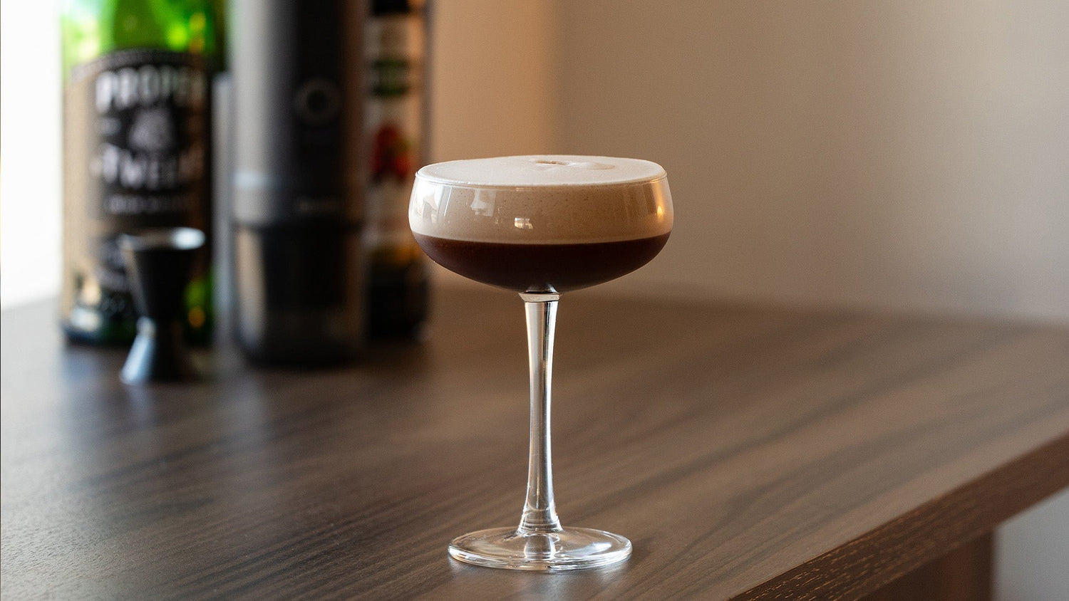 Elegant espresso martini with rich coffee-colored base and creamy foam top served in a stemmed coupe glass on wooden bar surface, demonstrating how coffee can be elevated into sophisticated cocktails.