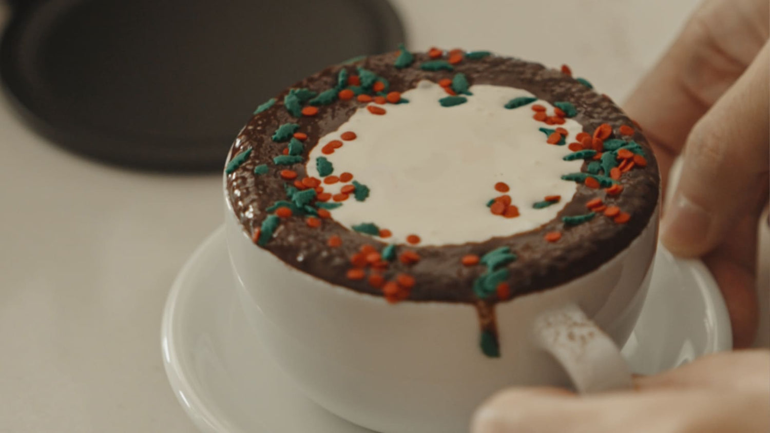 White coffee cup featuring chocolate topping with colorful red and green sprinkles arranged in a decorative pattern, perfect for holiday coffee variations beyond regular milk.