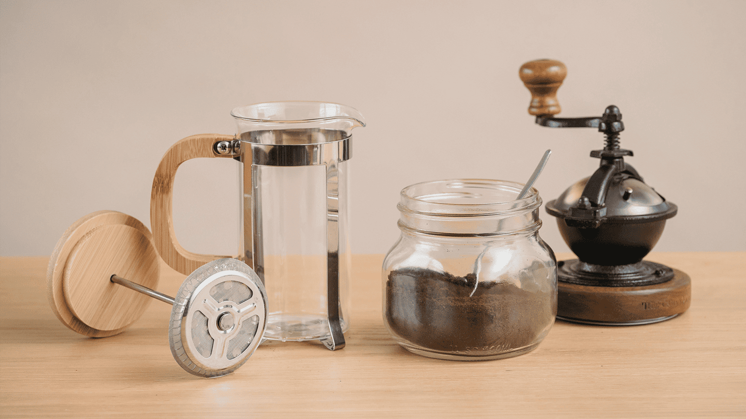 Complete manual brewing setup with French press, vintage hand grinder, and mason jar of coffee beans on wooden surface, rustic coffee preparation tools