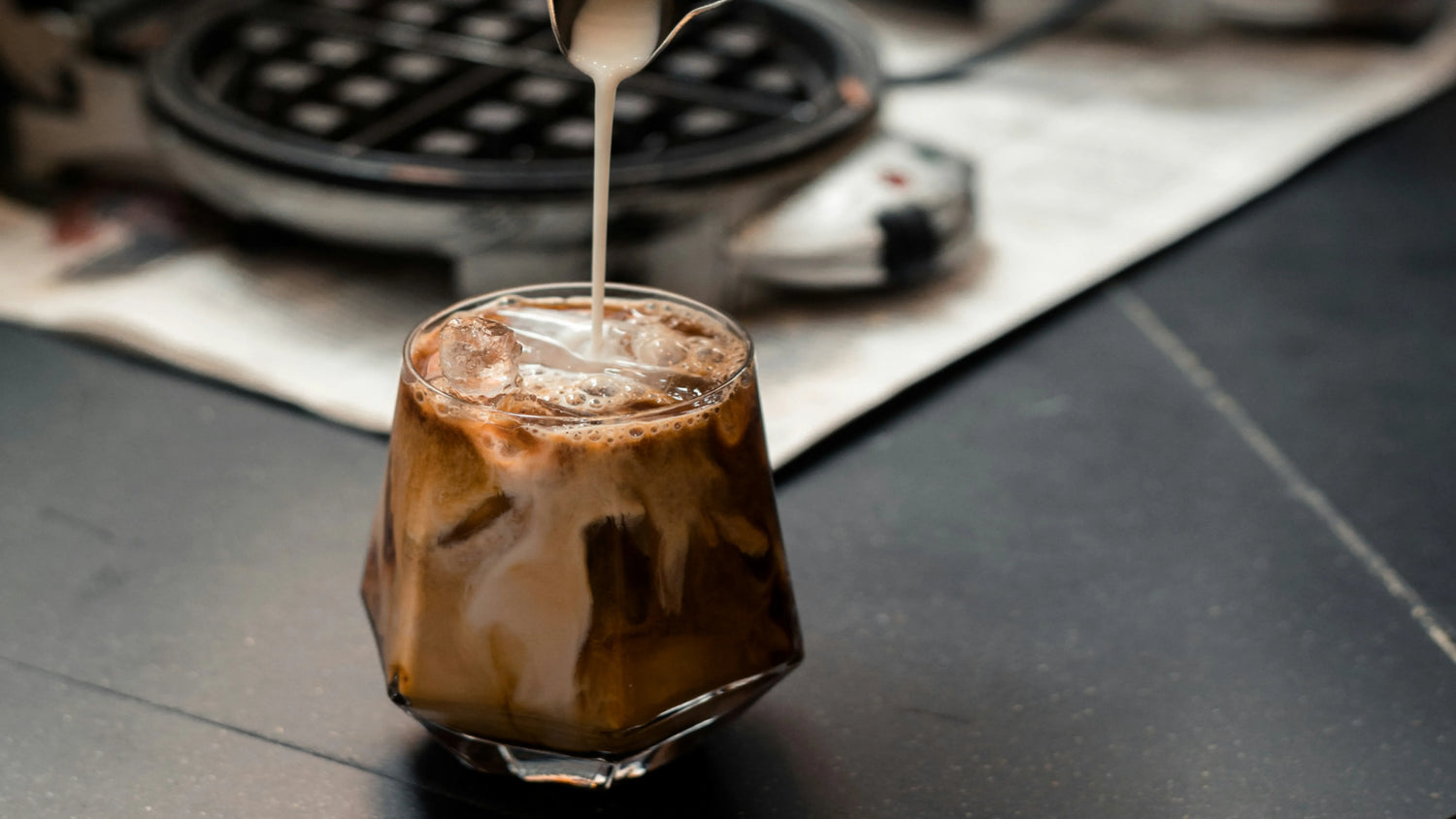 Close-up of an iced cappuccino with foamy milk poured over espresso in a glass.