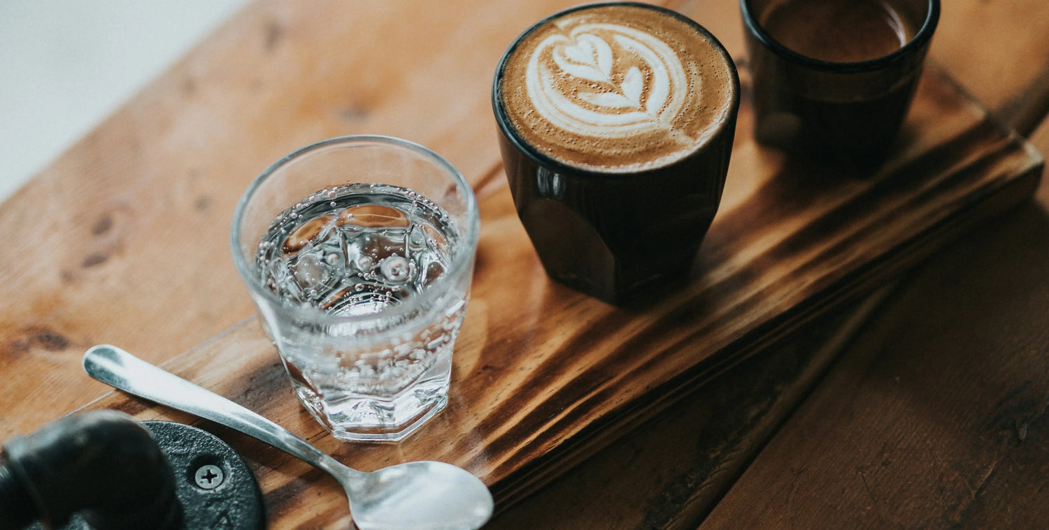 Latte with heart design, water glass, and spoon on wooden tray