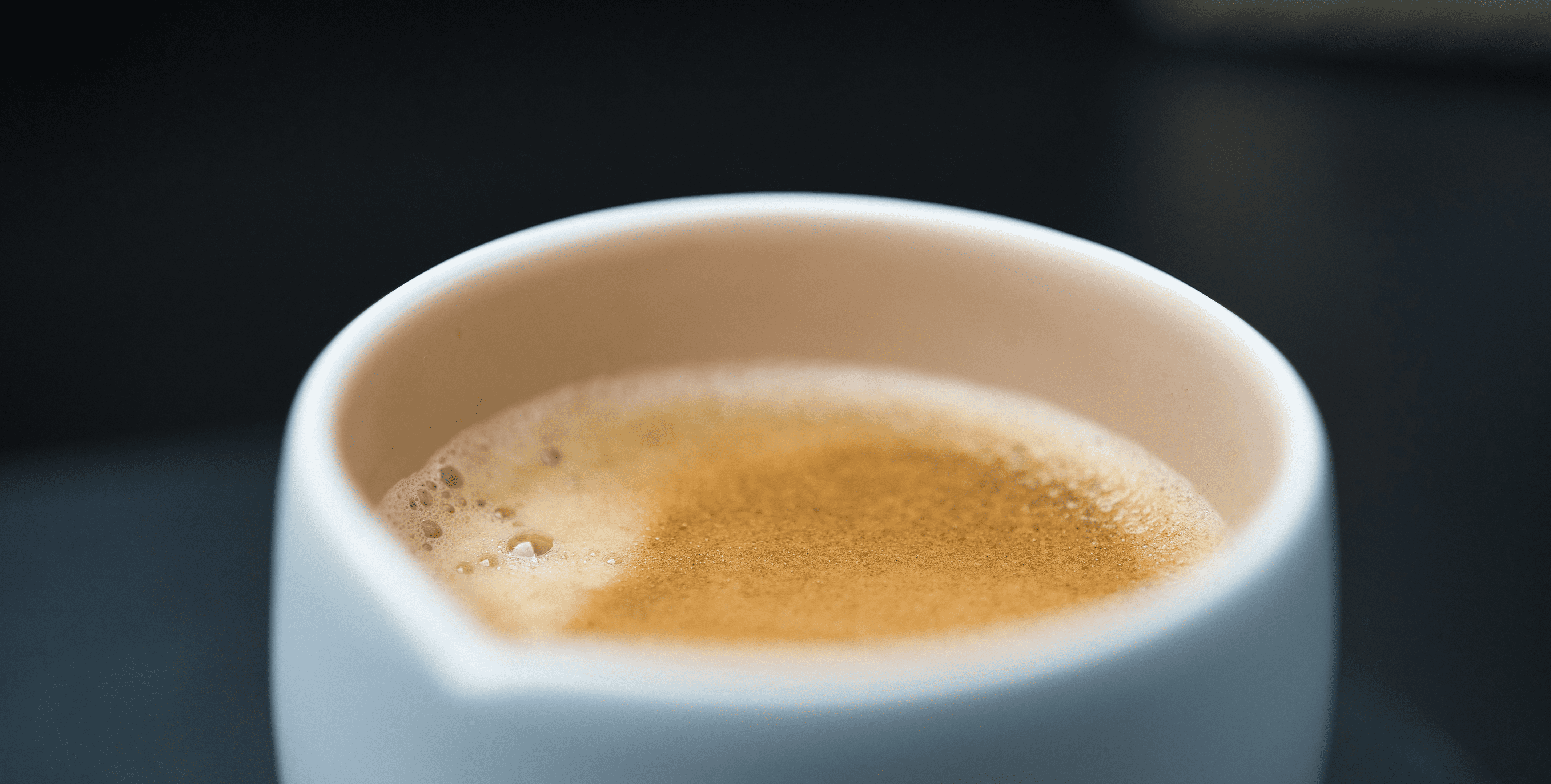 Close-up of freshly brewed espresso in white cup from Outin Nano, golden crema visible, dark background