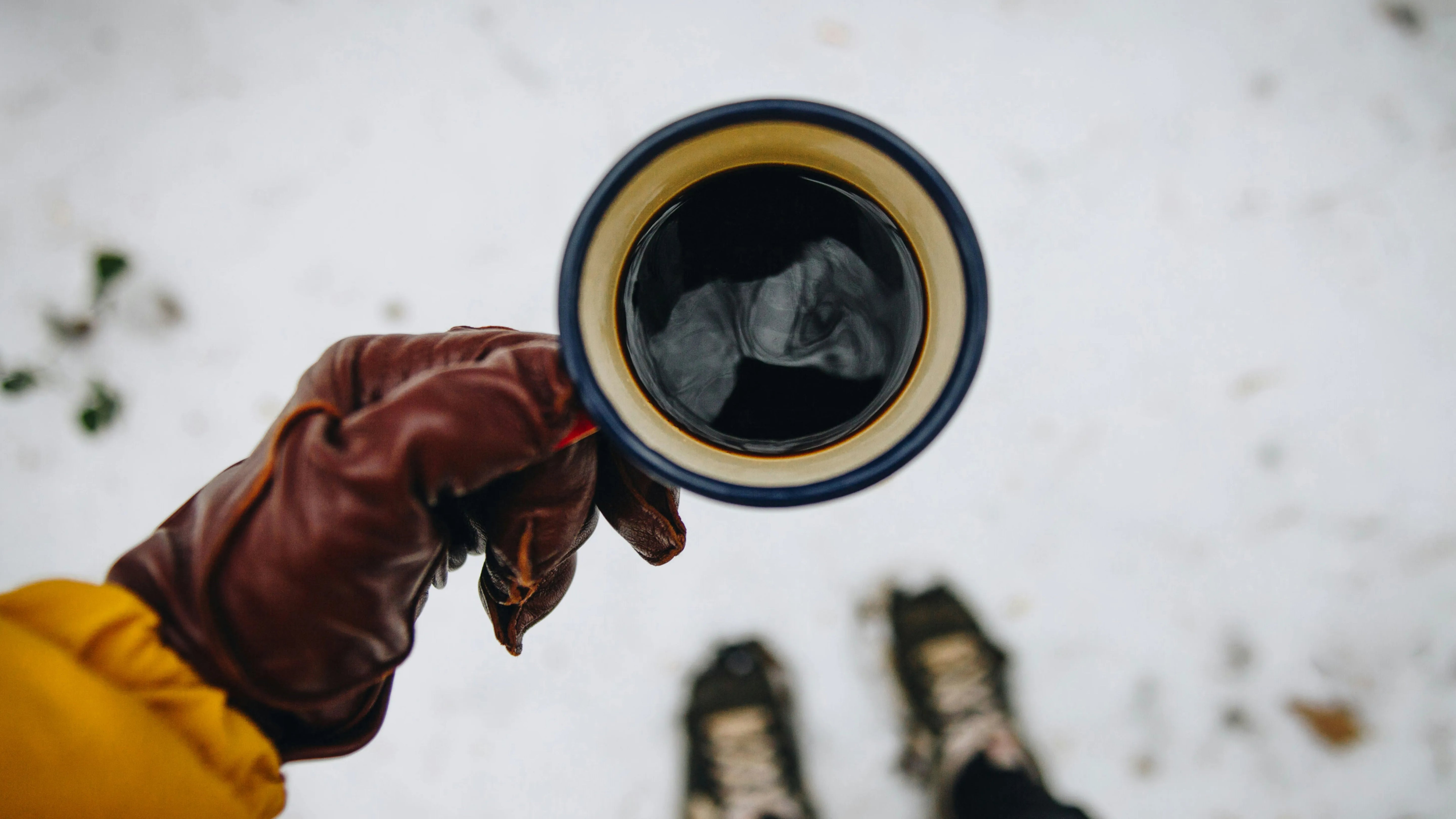 Portable espresso maker brewing hot coffee outdoors in winter, wearing leather gloves and yellow jacket, perfect for cold weather camping and hiking adventures with premium hand-pressed coffee maker