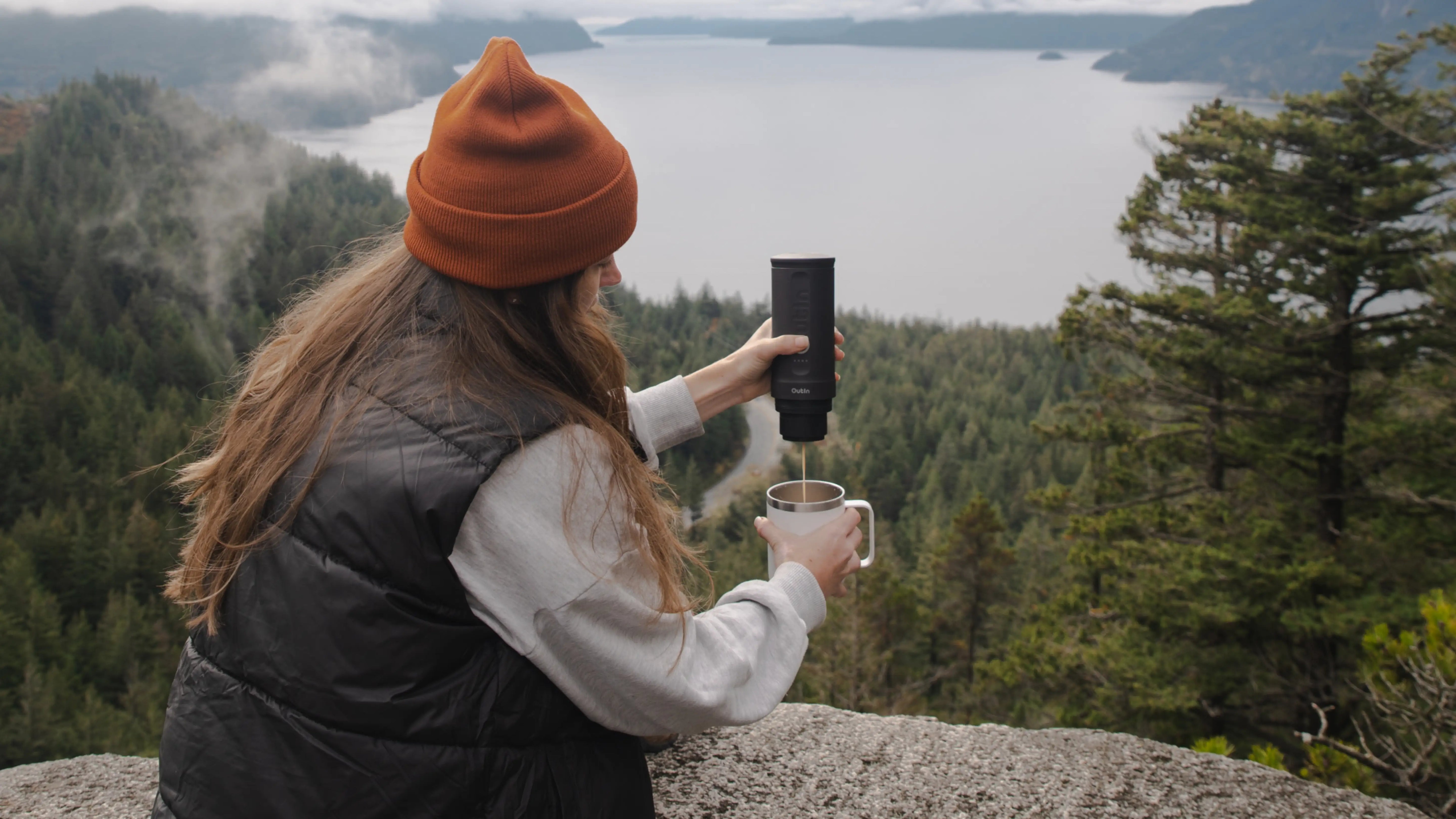 Person brewing fresh coffee with portable espresso maker while enjoying scenic mountain lake view, demonstrating outdoor coffee making convenience in nature