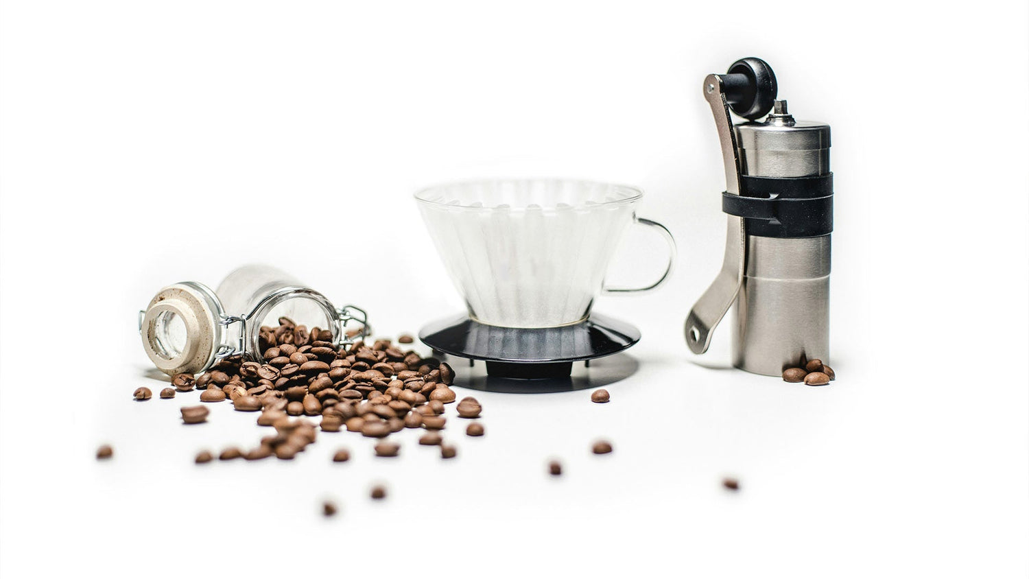 Complete pour-over coffee setup with manual grinder, glass dripper, and fresh coffee beans on white background, minimalist coffee brewing equipment display