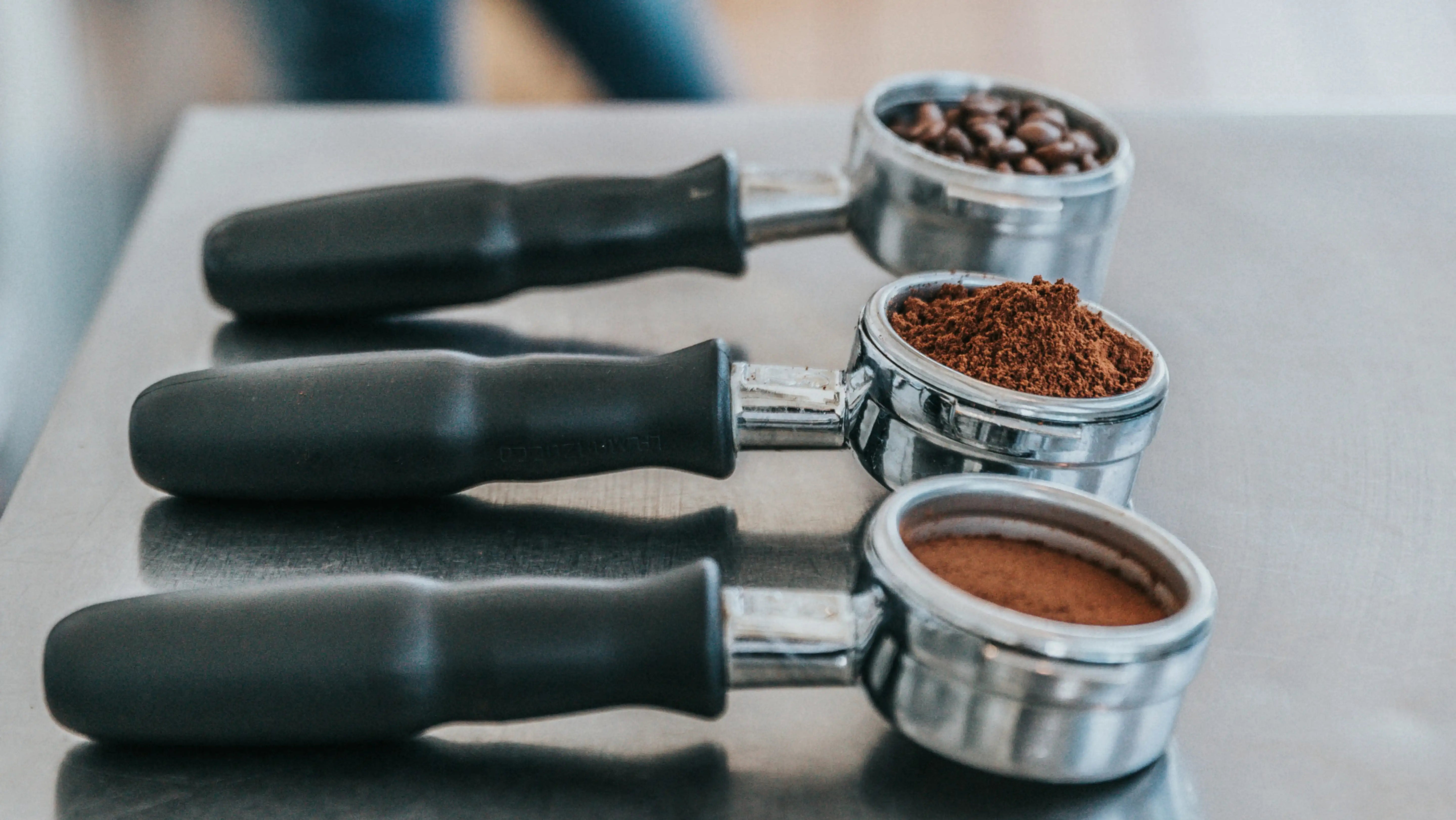 Three portafilters filled with coffee beans, ground coffee, and fine espresso grind