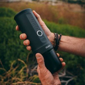 User holding Outin Nano Portable Espresso Machine outdoors in black.