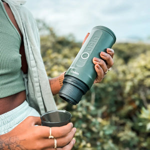 Person holding green Outin Nano Portable Espresso Machine in nature.