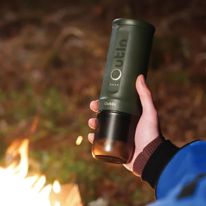 Person holding forest green Nano Portable Espresso Machine near campfire.